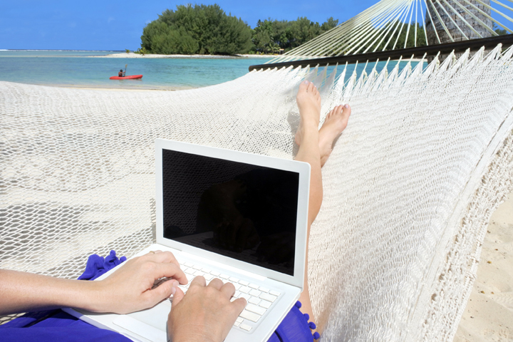 POV of a woman lay on a hammock working on a laptop while her man kayaking in Muri lagoon in Rarotonga, Cook Islands. Real people. Copy space