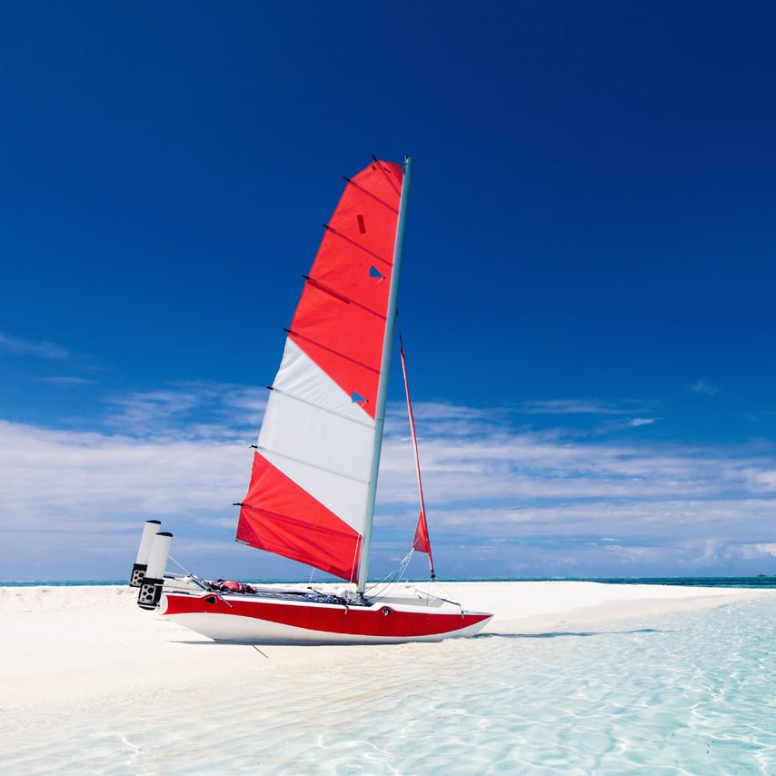 Sailing boat with red sail on a beach of deserted tropical island with shallow blue water